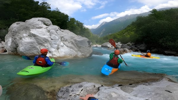 Estudiantes de la Coláiste Naomh Cormac reman en coloridos canoas en un río con un entorno verde y acantilados rocosos.