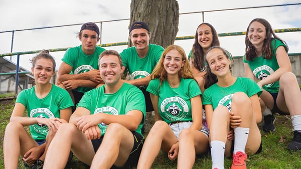 Un grupo de estudiantes del College Bourget está sentado al aire libre juntos y sonriendo frente a un fondo de madera.