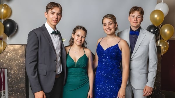 Cuatro estudiantes del Collège de Sainte-Anne-de-la-Pocatière posan formalmente frente a una pared brillante decorada con globos.