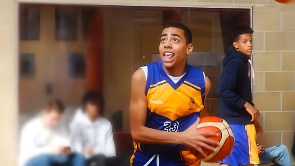 Un estudiante del College of Richard Collyer sostiene un baloncesto en un gimnasio con otras personas al fondo.