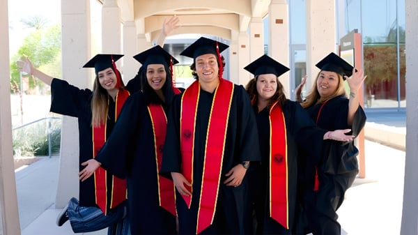 Cinco graduadas en togas están frente al edificio del College of the Desert.