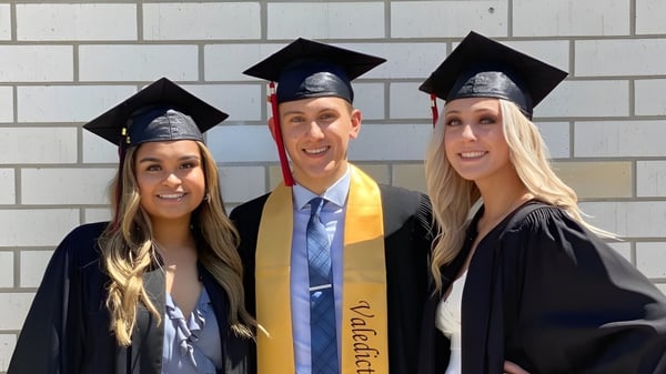 Tres graduados en ropa de graduación posan frente a una pared de ladrillos en el campus del Collège Pierre-Elliott-Trudeau.