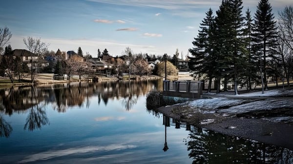 Un tranquilo lago invernal refleja los edificios y árboles en el terreno del Collège Pierre-Elliott-Trudeau.