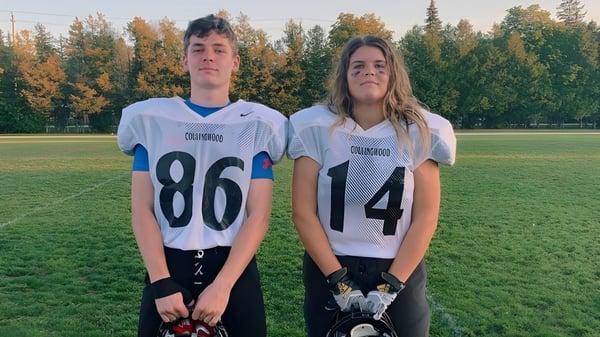 Dos estudiantes del Collingwood Collegiate Institute están de pie en camisetas deportivas en un prado con un bosque al fondo.