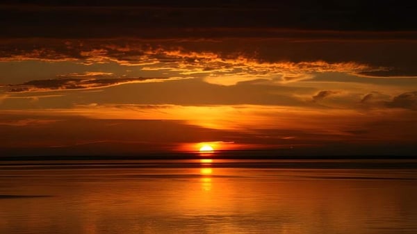 Un atardecer con cielo anaranjado se refleja tranquilamente en el agua cerca de la Colonel Gray High School.