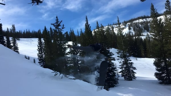 Un esquiador se desliza por un paisaje montañoso cubierto de nieve con pinos en primer plano en el terreno de la Colorado Rocky Mountain School.