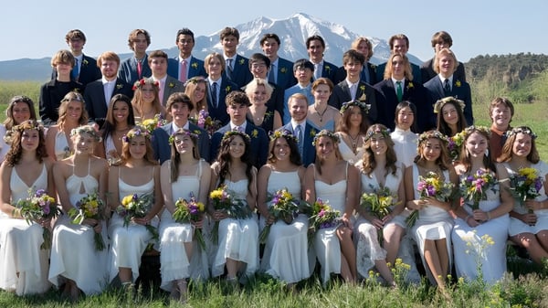 Un gran grupo de estudiantes de la Colorado Rocky Mountain School está vestido formalmente frente a un telón de fondo de montañas cubiertas de nieve.