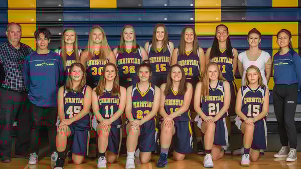 Un grupo de jóvenes jugadoras de baloncesto posan frente a un colorido fondo amarillo y azul en el campus de la Colorado Springs Christian School.