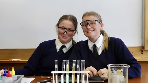 Dos alumnas en uniformes escolares posan sonriendo en un aula del Columba College.