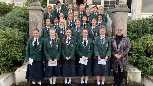 Un grupo de alumnas en uniformes verdes está frente a un edificio de piedra en el campus del Columba College.