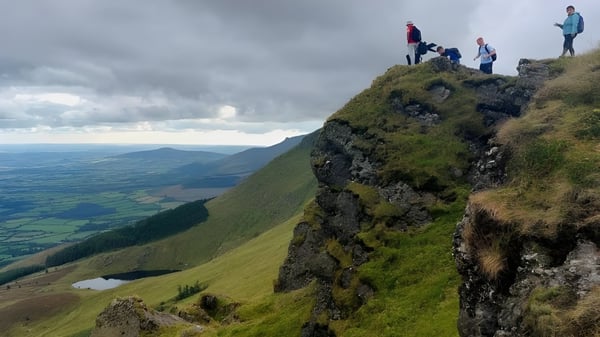 Estudiantes del Comeragh College están en un acantilado cubierto de musgo mirando hacia un valle verde con montañas al fondo.