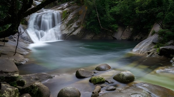 Una cascada fluye sobre terreno rocoso en medio de la naturaleza verde sin relación directa con Como Secondary College.