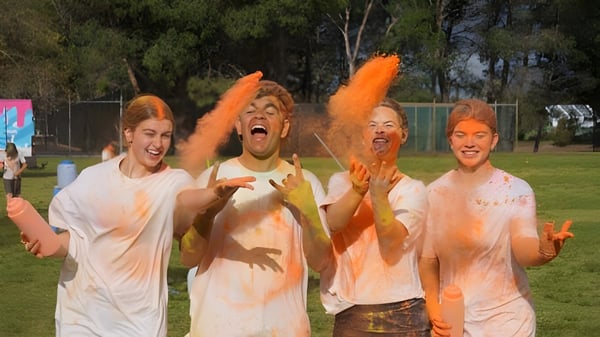 Estudiantes del Como Secondary College lanzan polvo naranja al aire al aire libre durante un evento.