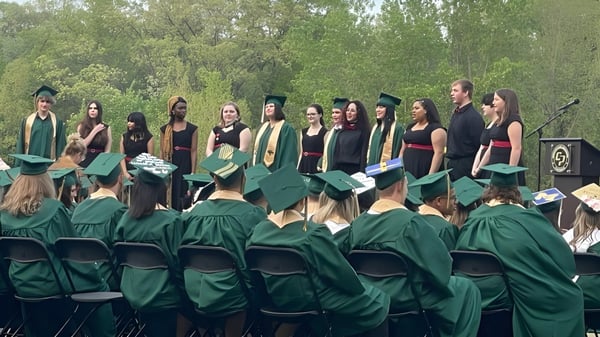 Un grupo de graduados de la Comstock Park High School está afuera en togas verdes rodeados de árboles.