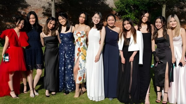 Un grupo de jóvenes mujeres del Concord College posan frente a una pared de ladrillo con vegetación alrededor.