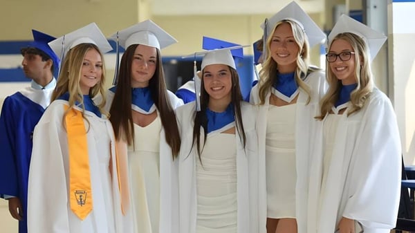 Un grupo de estudiantes de la Conwell-Egan Catholic High School está de pie en vestidos y birretes blancos y posan para una foto.