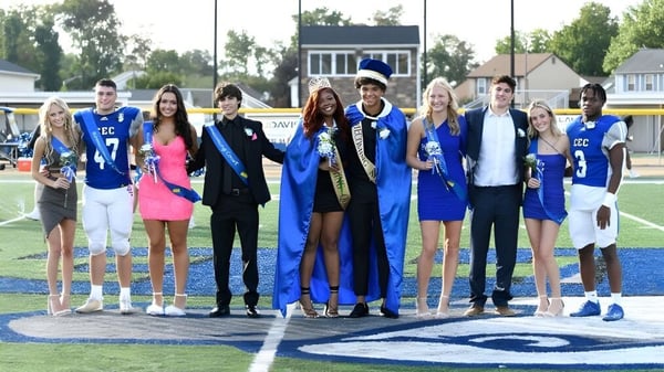 Un grupo de graduados de la Conwell-Egan Catholic High School está de pie en un campo deportivo con edificios y árboles de fondo.