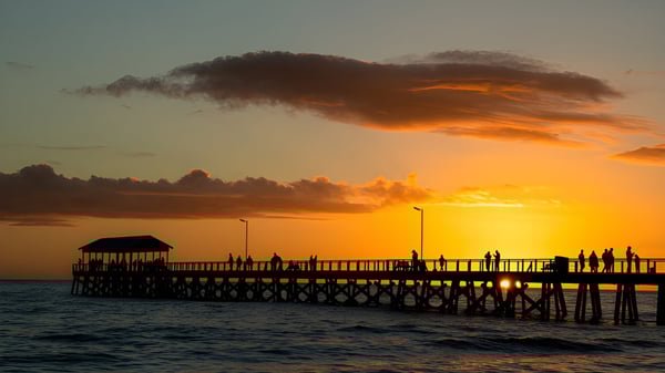 Un muelle de madera se extiende durante el atardecer con nubes dramáticas sobre el agua en el terreno de la Coolum State High School.