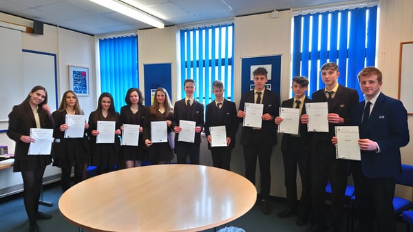 Estudiantes de la Corfe Hills School en el aula con persianas azules sosteniendo sus certificados.