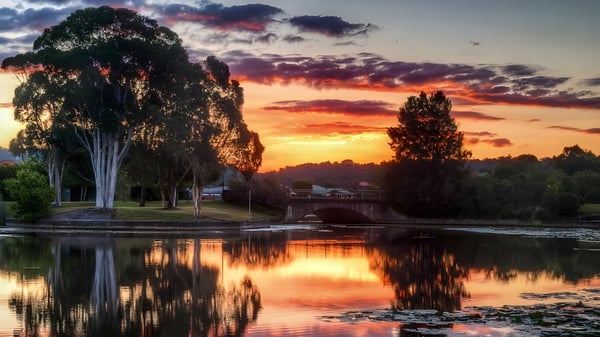 Un tranquilo lago con sauce y plantas ribereñas refleja el atardecer cerca de la Corinda State High School.