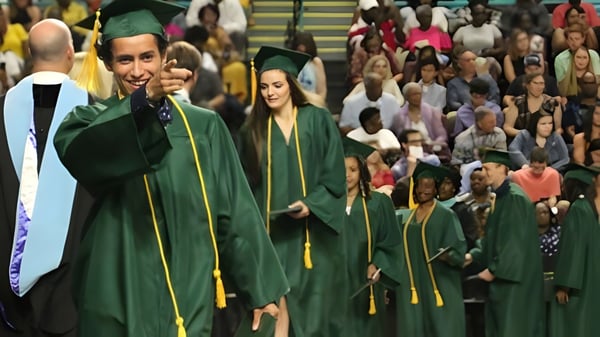 Un grupo de graduadas y graduados de la Corinda State High School en togas verdes caminan juntos frente a un gran público.
