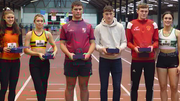 Alumnos de la Cork Educate Together Secondary School están en una pista cubierta mostrando sus trofeos y medallas ganados.