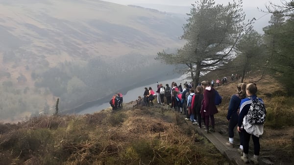 Un grupo de alumnas y alumnos de la Cornafulla National School camina por un sendero a través de un paisaje montañoso con un río al fondo.
