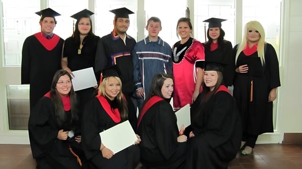 Un grupo de graduados y graduadas de la Cornwall Collegiate & Vocational School posan con vestimenta académica frente a grandes ventanas.