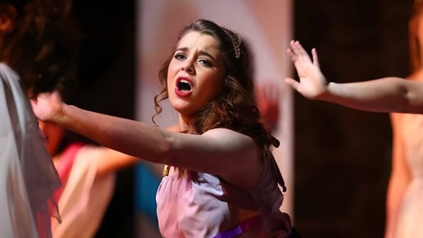 Una estudiante de la Covenant Christian High School canta en el escenario frente a un fondo colorido.