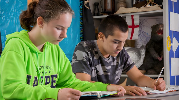 Dos estudiantes de la Covenant Christian School leen y escriben concentrados en un acogedor interior.
