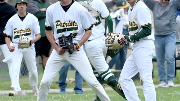 Un grupo de jugadores de béisbol en uniformes blancos y verdes está de pie en el campo de Coventry High School.