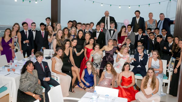 Un grupo de personas vestidas de manera formal se reúne en una fiesta en el Cranbrook Education Campus bajo luces de cadena.
