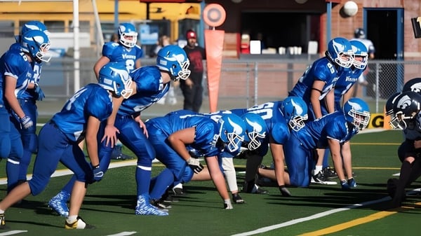 Alumnos de la Crescent Heights High School se reúnen en camisetas azules en el campo de fútbol con un edificio al fondo.