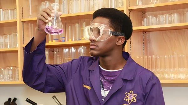Un estudiante de la Crescent Heights High School sostiene en un laboratorio un vaso con líquido rosa frente a una estantería.