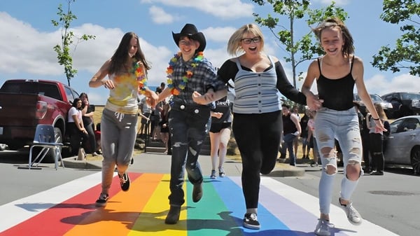 Un grupo de jóvenes estudiantes de la Creston Valley Secondary School camina sobre una alfombra roja frente a vehículos bajo un cielo nublado.