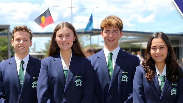 Cuatro estudiantes de la Cronulla High School están frente a un fondo con banderas.