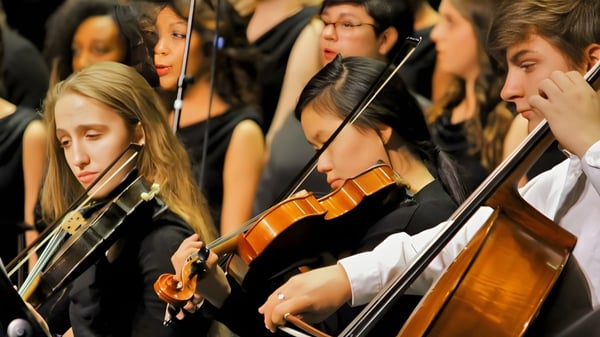 Un grupo de estudiantes de la Crowsnest Consolidated High School toca varios instrumentos de cuerda en un escenario.