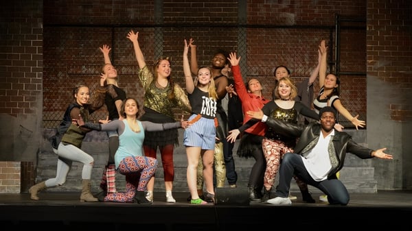 Un grupo de estudiantes de la Cushing Academy posan frente a una pared de ladrillo con los brazos en alto.