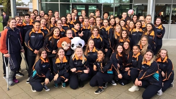 Un grupo de estudiantes de Dalyellup College está en uniformes negros y naranjas uniformes frente a un moderno edificio de vidrio.