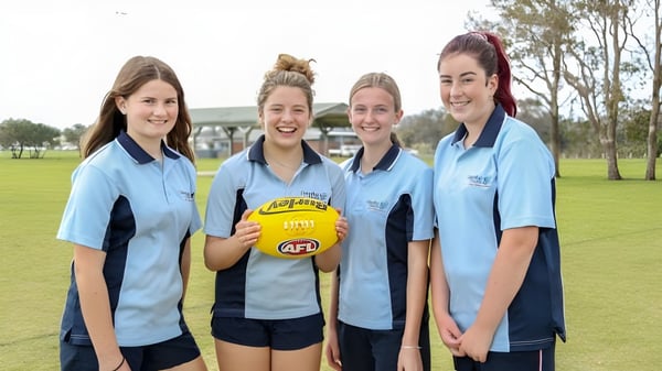 Cuatro estudiantes de Dalyellup College están juntas en un campo de césped sosteniendo un balón de Australian Rules Football.