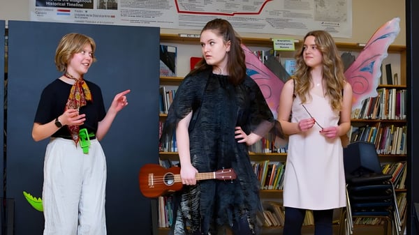 Tres estudiantes del Daniel McIntyre Collegiate Institute están con un ukelele en una habitación con estanterías.