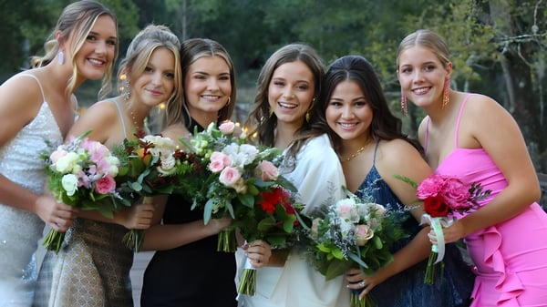 Un grupo de estudiantes sonrientes de la Darlington School está con ramos de flores en un área exterior verde.