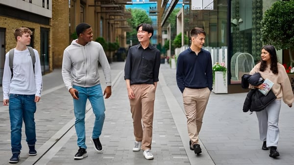 Un grupo de estudiantes del David Game College camina juntos por una calle con edificios y tiendas.