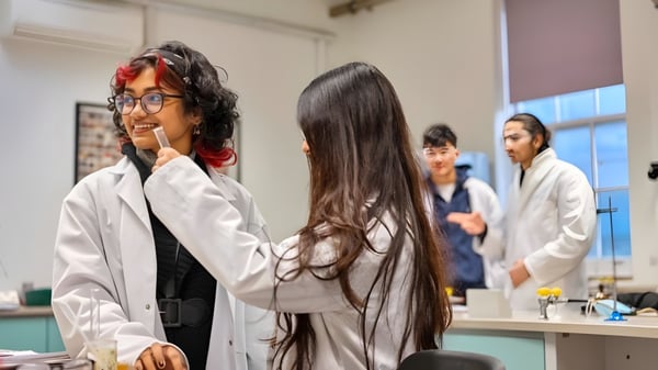 Estudiantes del David Game College trabajan en un laboratorio con batas de laboratorio y gafas de protección.