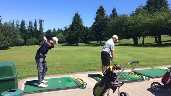 Dos golfistas están en el campo de golf en el área verde del campus de la David Thompson Secondary School.