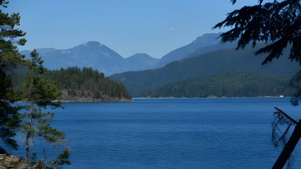 Un tranquilo lago alpino con montañas cubiertas de nieve y bosques perennes frente al telón de fondo de la David Thompson Secondary School.