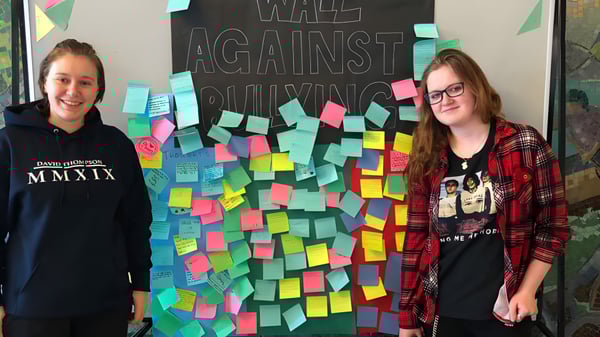 Dos estudiantes están frente a la pared anti-bullying con notas coloridas en la David Thompson Secondary School.