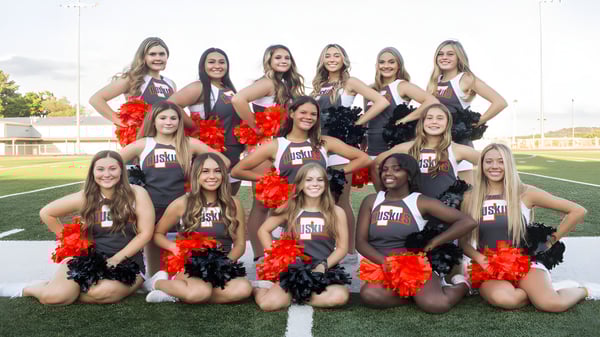 Un grupo de animadoras en uniformes uniformes posan en el campo deportivo del Davis School District.