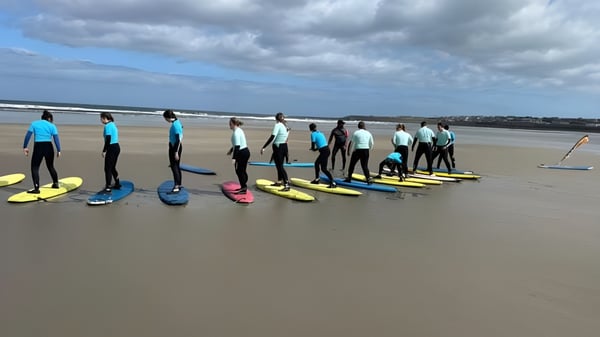 Estudiantes del Davitt College participan en el curso de surf en la playa bajo un cielo nublado.