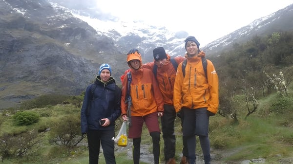 Un grupo de estudiantes del De la Salle College (Macroom) está en una caminata con coloridos impermeables en un paisaje montañoso con picos cubiertos de nieve.